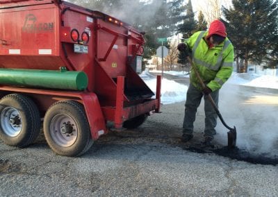 A Falcon worker spreads hot mix asphalt over a pothole.