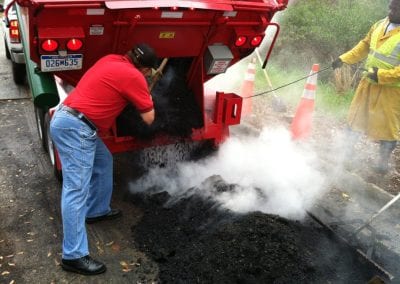 A worker shoveling hot mix asphalt from a hot box into a pothole for repair.